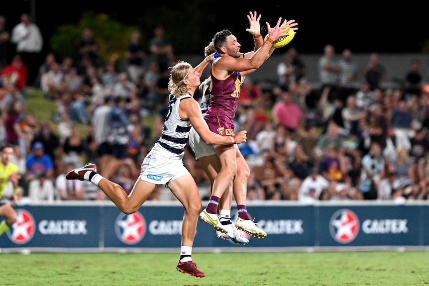 A Brisbane Lions forward flies to grab the ball as a Geelong defender tries to grab from behind.