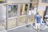 A still from a CCTV camera showing a male cleaner near the damaged glass doors of a gym.