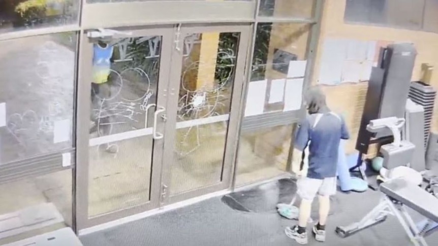 A still from a CCTV camera showing a male cleaner near the damaged glass doors of a gym.