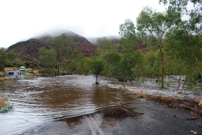 a road cut off by floodwaters with mountains in the background