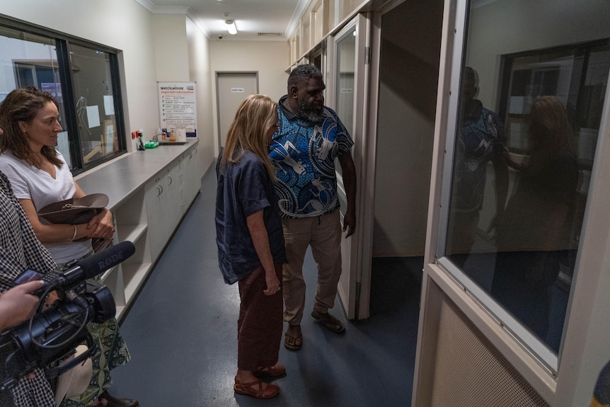 A woman and man stand at the door of a police cell. 