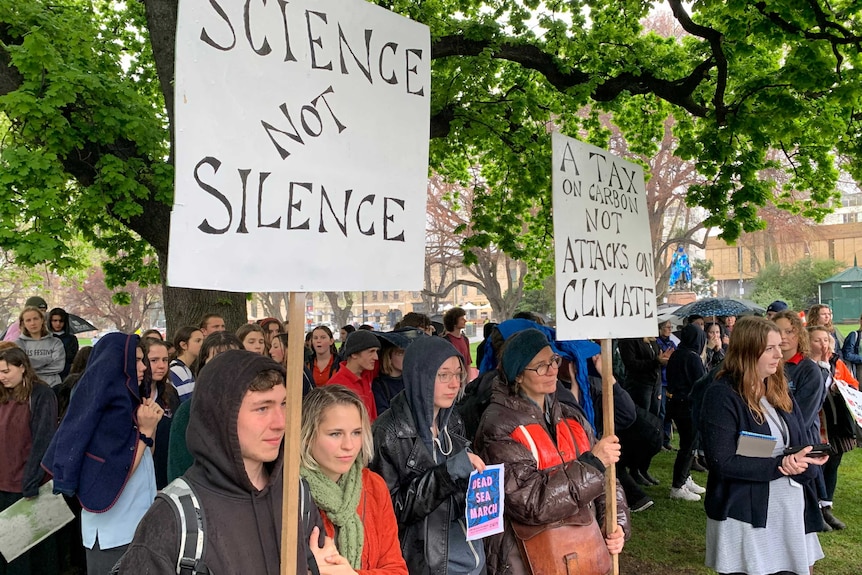 About 100 people stand under the rain, some hold placards urging climate change action.