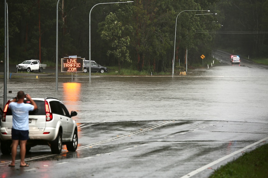A flooded road, a police car to the right and a man taking a photograph