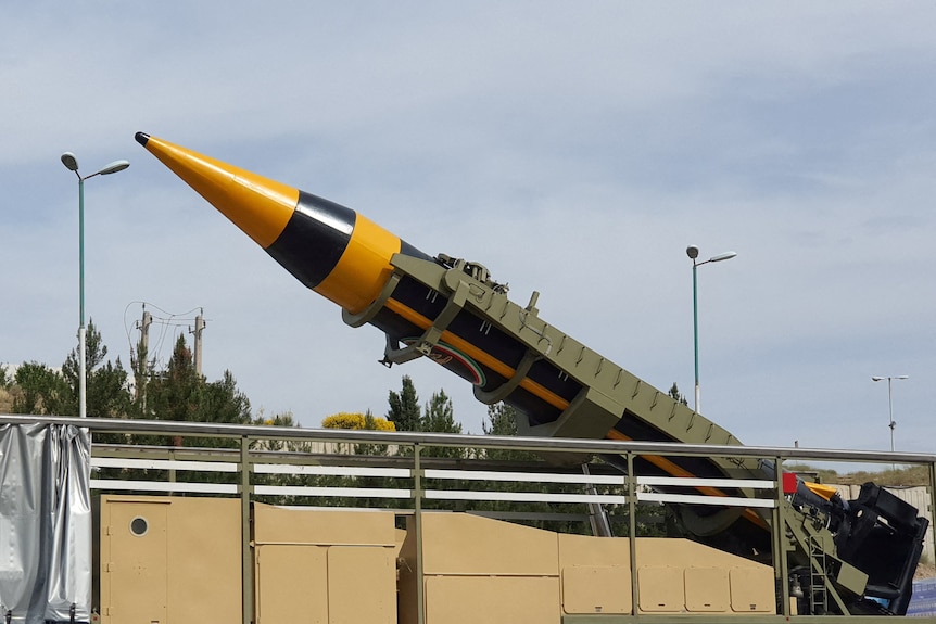 A yellow and black cylindrical ballistic missle sits in a green metal launcher at a 45 degree angle.