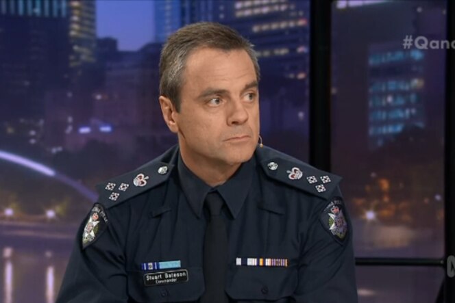 Stuart Bateson, wearing a police uniform looks to his left while sitting on the set of Q&A