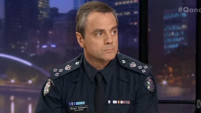 Stuart Bateson, wearing a police uniform looks to his left while sitting on the set of Q&A