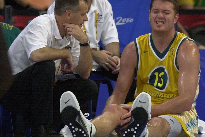 Luc Longley has a pained face as he holds his injured ankle