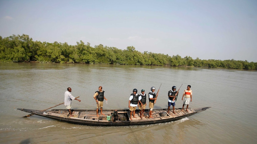 Wide shot of a group of men with guns standing on a boat on a river.
