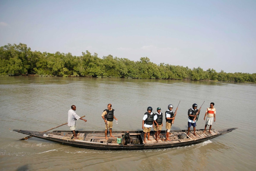 Wide shot of a group of men with guns standing on a boat on a river.