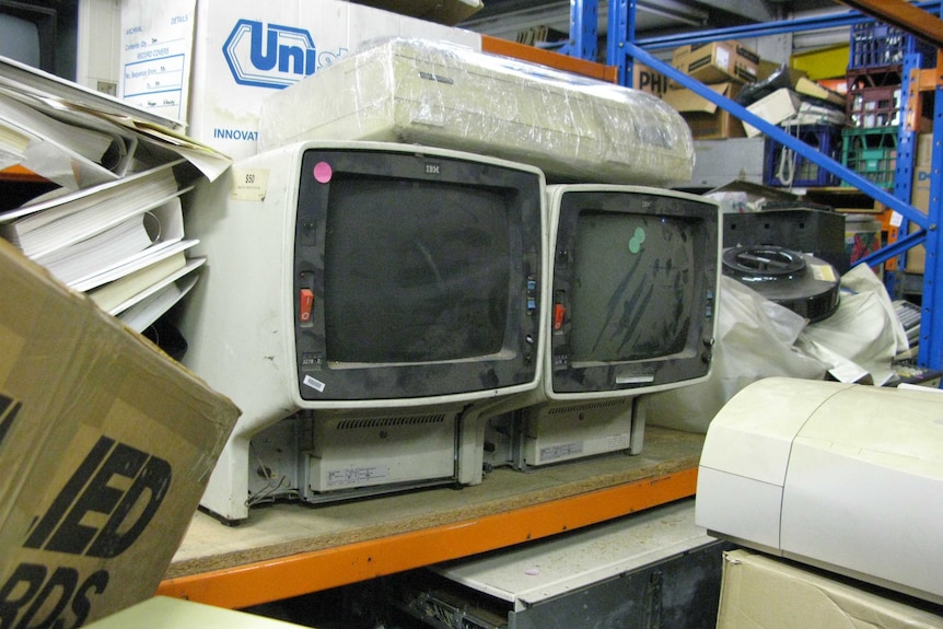 Two old computers surrounded by boxes.