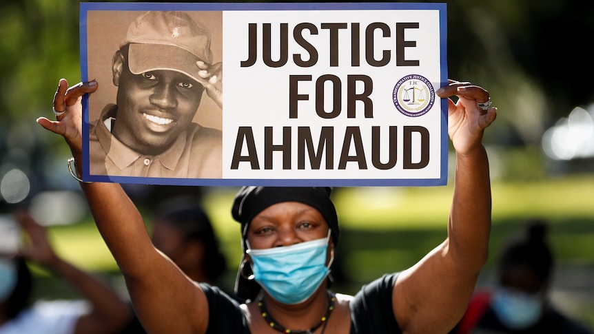 A woman holds a sign saying "Justice for Ahmaud"