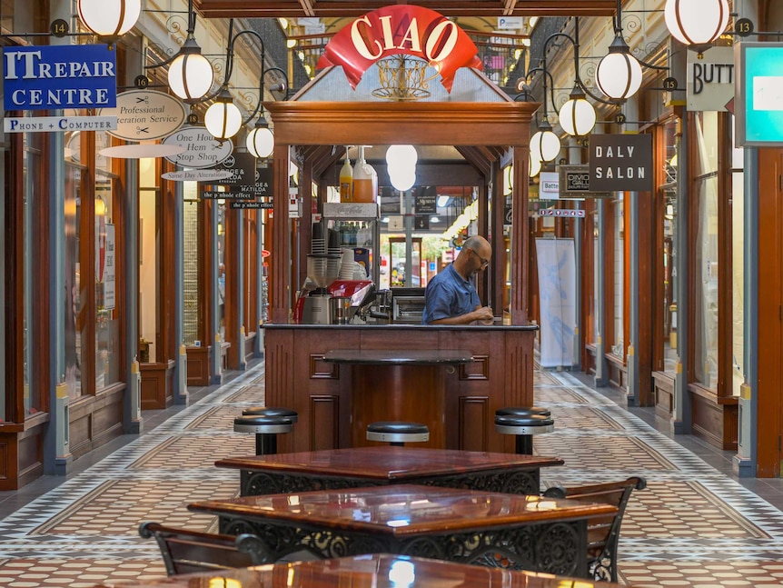 A barista waits in his coffee stand for customers in an empty Adelaide Arcade.