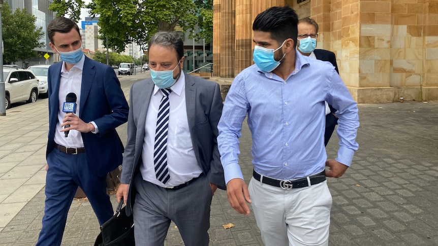 Four men leave court walking side-by-side dressed in formal shirts and suits.