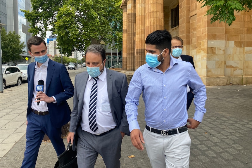 Four men leave court walking side-by-side dressed in formal shirts and suits.