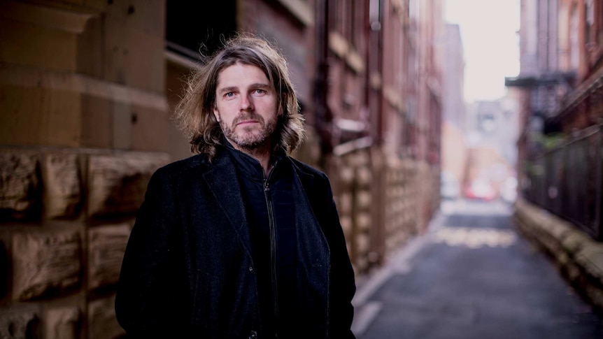 A middle aged man stands in a city alleyway.