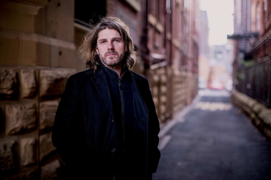 A middle aged man stands in a city alleyway.