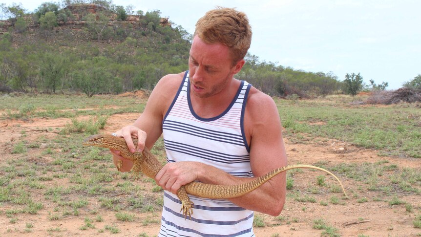 A man holds a sand goanna in the bush.