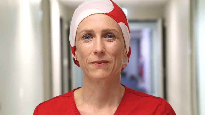 A surgeon wearing red scrubs and a red and white headscarf.
