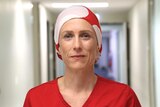 A surgeon wearing red scrubs and a red and white headscarf.