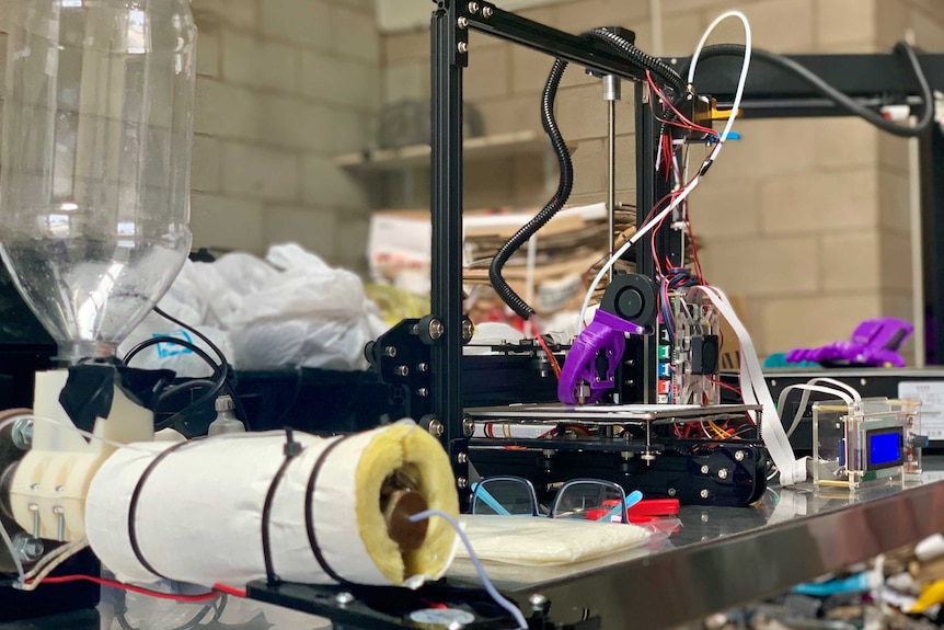 A small plastic extruder sits on a bench next to a 3D printer