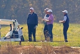 Donald Trump stands on a golf course with three other men.