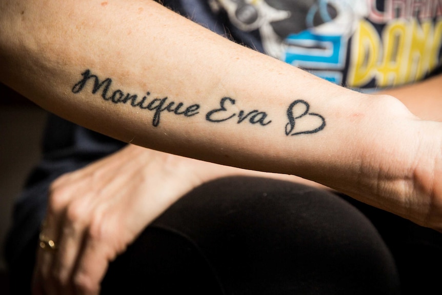 An arm is tattooed with Monique Eva and a heart.