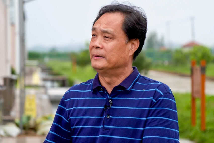 A man in a polo shirt stands outside a factory building