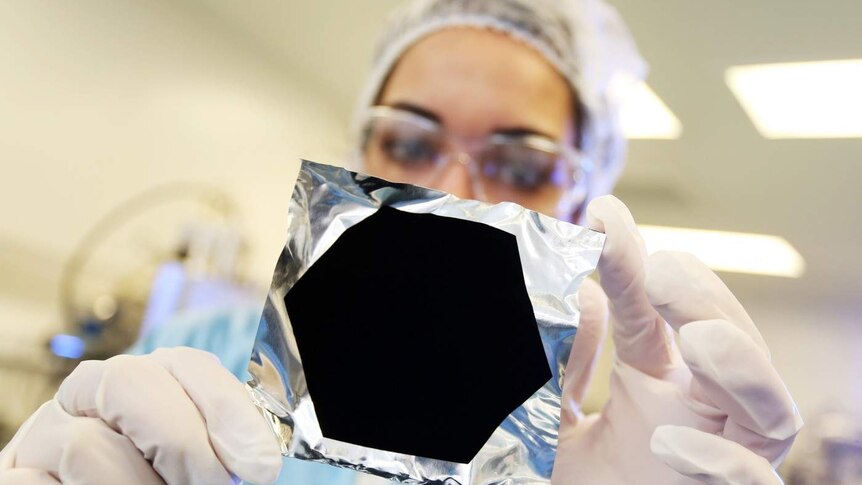 A woman holds up a piece of foil with a Vantablack coating on it