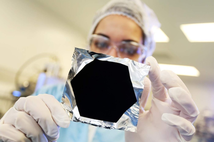 A woman holds up a piece of foil with a Vantablack coating on it