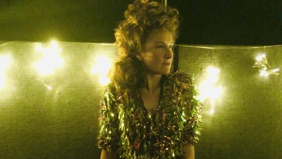 singer poses thoughtfully in outlandish, gold, sequinned jumpsuit