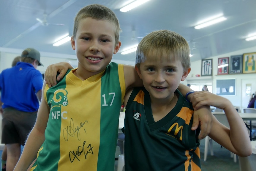 Two children wearing autographed green and gold football guernseys stand arm in arm, smiling at the camera.