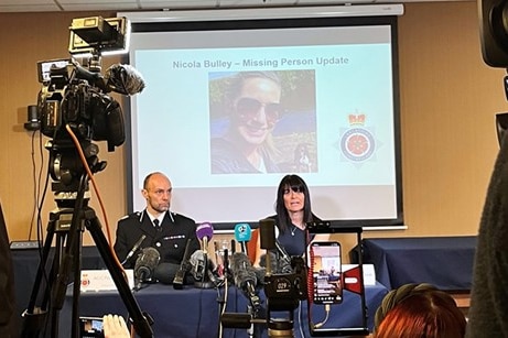 Peter Lawson and Rebecca Smith sit at a table in front of microphones and cameras, with a photo of Nicola Bulley