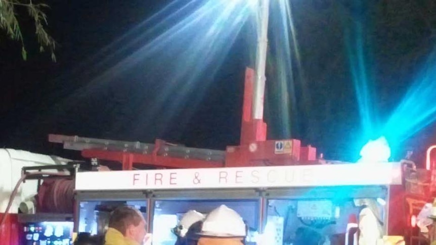 Three WA firefighters (back to camera) at night with fire engine in background with lights on