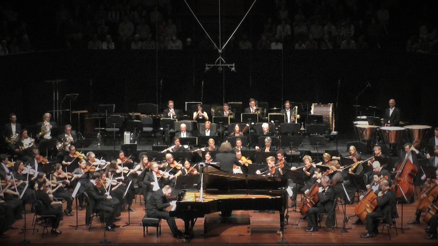 Pianist Lukáš Vondráček sits at the piano in front of conductor Asher Fisch and the West Australian Symphony Orchestra.