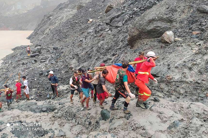 Rescuers carry a recovered body of a victim of a landslide as a muddy lake is seen in the background.