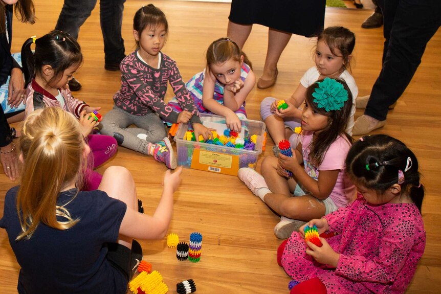 A group of young children gather around a box full of colourful toys on the floor