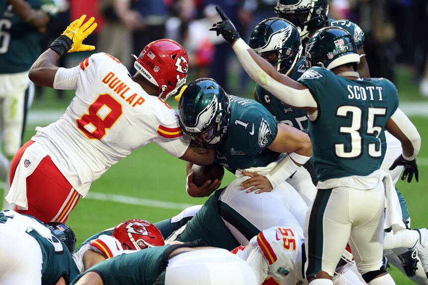 A Philadelphia Eagles quarterback barges into the end zone with the ball as a Kansas City Chiefs defender tries to stop him. 