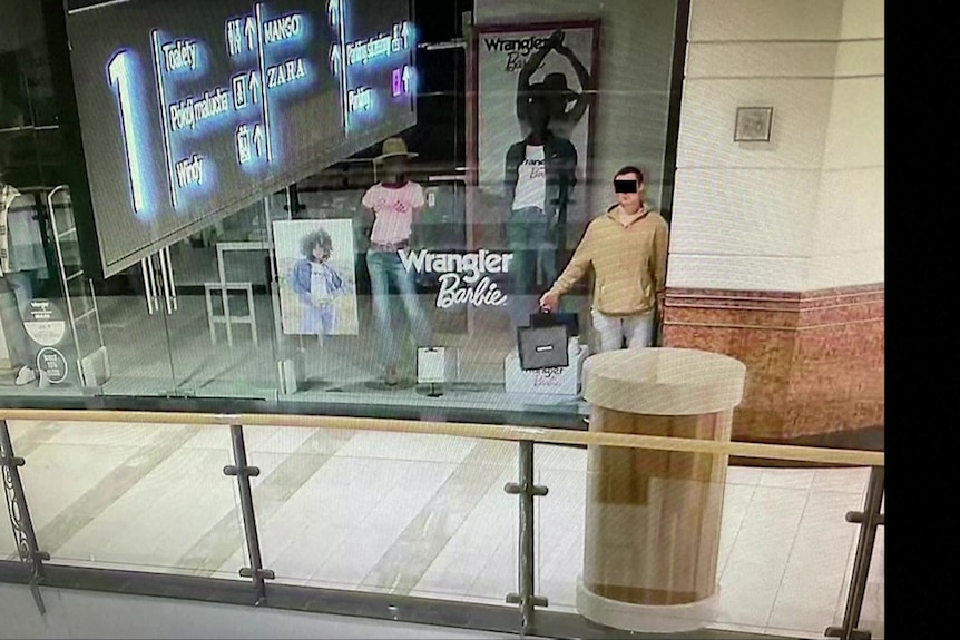 A man poses in a shop window in Poland before allegedly stealing jewellery, food and clothing.