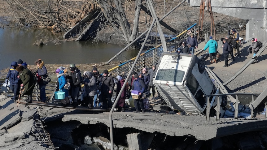 People cross an improvised path under a destroyed bridge