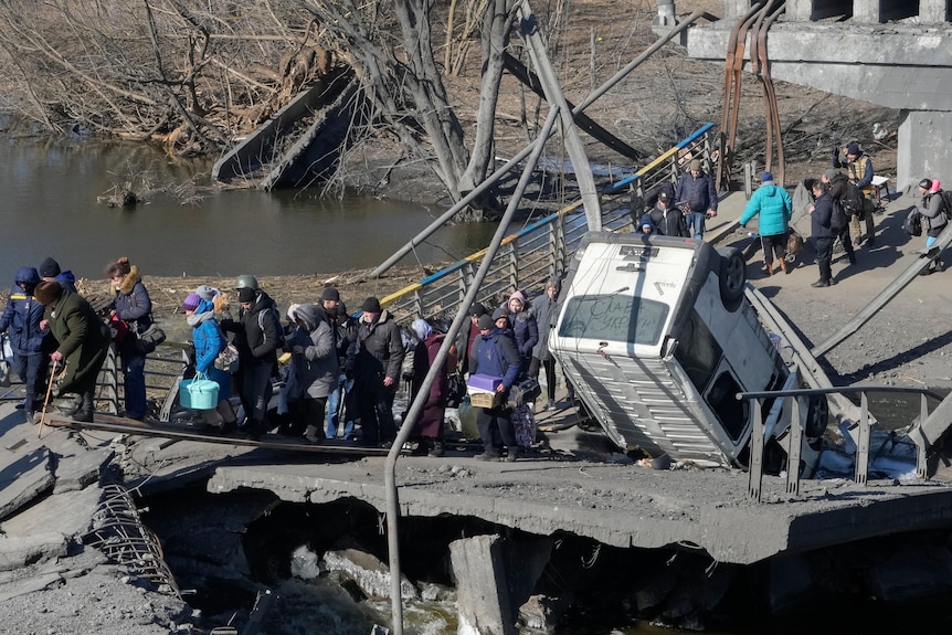 People cross an improvised path under a destroyed bridge