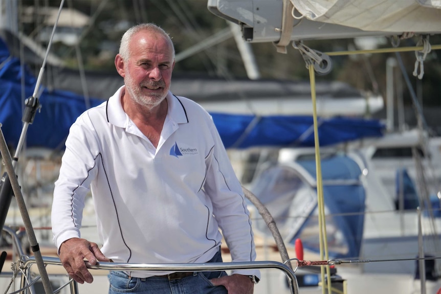 A man stands on a yacht in a marina.