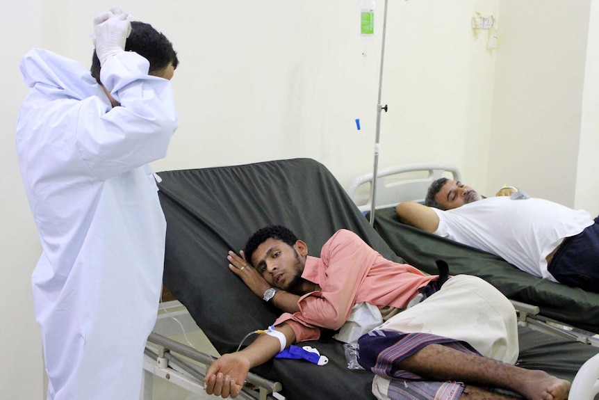 A Yemeni doctor talks to a patient laying on a hospital bed.