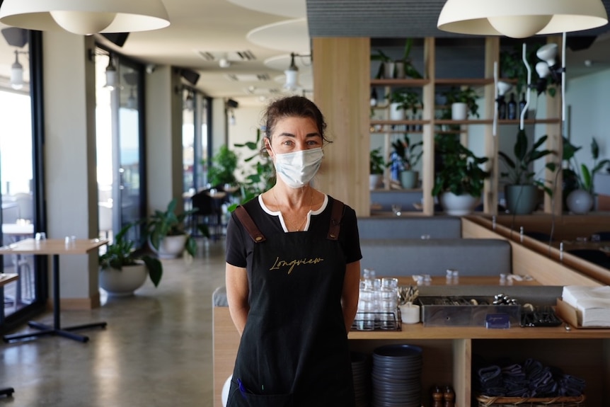 A wide shot of Jodie standing in the middle of the restaurant with a mask on