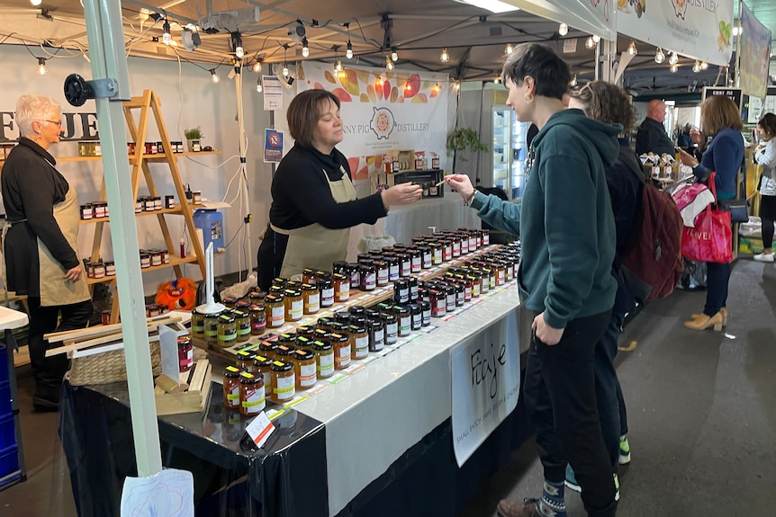 woman dealing with customers with her table display of jams at a farmers market