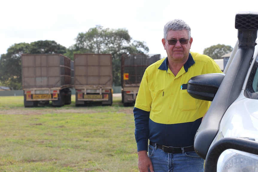 A man in a high-vis shirt leans against a ute with sugarcane trucks behind