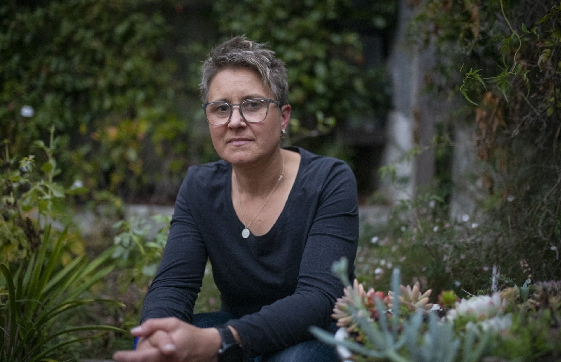 A woman with short hair wearing a black shirt while sitting in a garden.