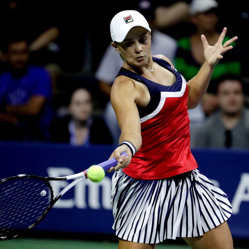 A female tennis player wearing a red top and white hat hits a forehand
