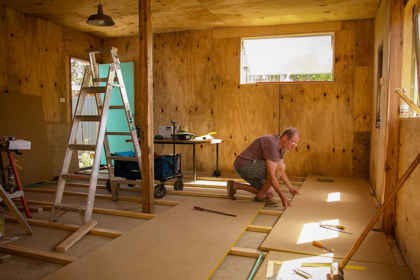 Don Ashby kneels to place flooring down in the wooden frame on his new house.