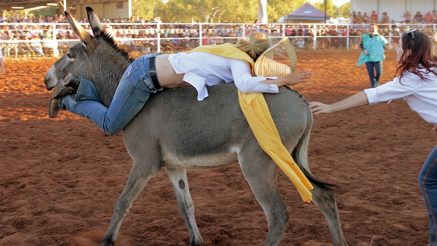 A girl lies backwards on a donkey, with her legs entwined around its neck, in a bid to stay on during one event.