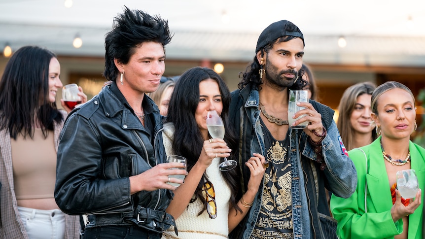 A group of young fashion-conscious people stand together outdoors holding drinks
